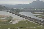 A distant view of ‘Mountaineer’ & ‘Moelwyn’ running along the Cob towards Porthmadog with a long train.       (01/05/2005)